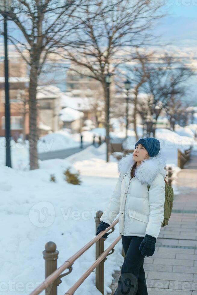 mujer turista visitando en hakodate, viajero en suéter Turismo hachiman zaka Pendiente con nieve en invierno. punto de referencia y popular para atracciones en Hokkaidō, Japón. viaje y vacaciones concepto foto