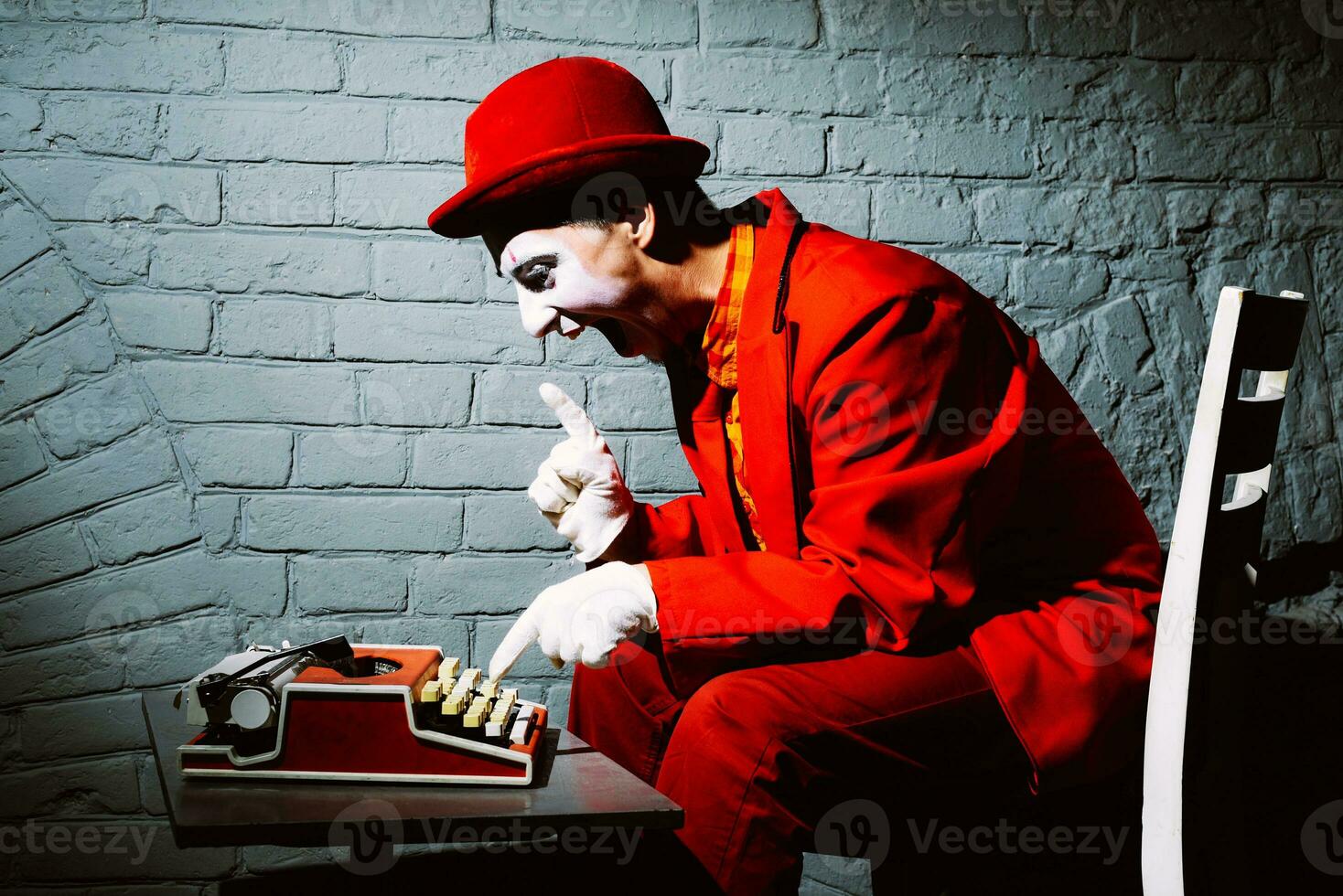 Mime in a red suit prints on a typewriter photo