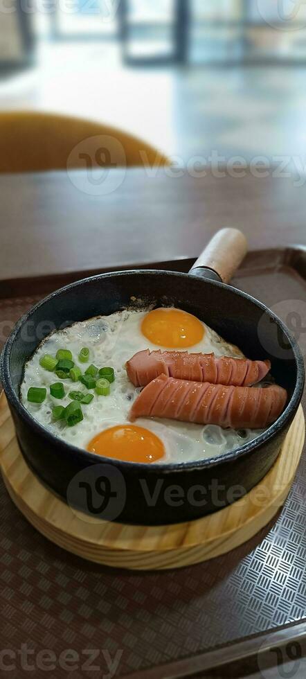 Scrambled eggs in a frying pan with fried meat sausages photo