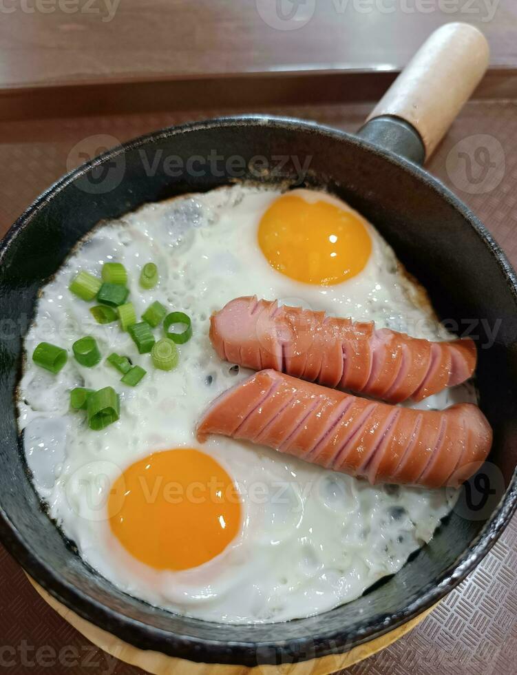 Scrambled eggs in a frying pan with fried meat sausages photo