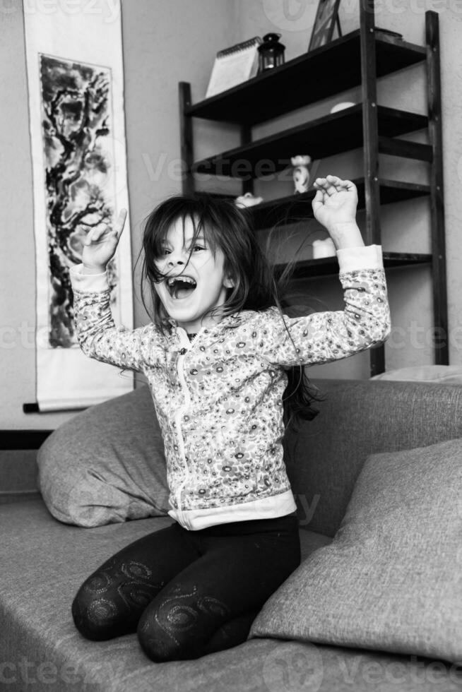 little girl jumps on a sofa in the room photo