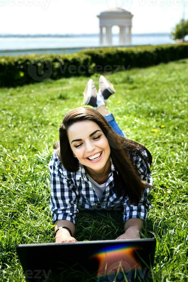 hermosa niña sentado en el parque con un ordenador portátil foto