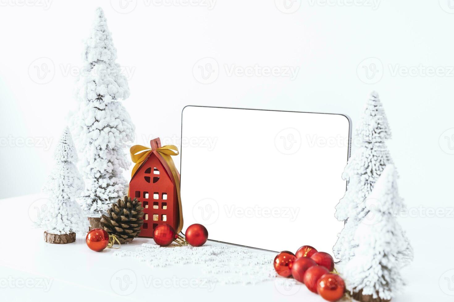 Tapelet with a white screen mock-up and White calendar with a festive scene of a beautiful Christmas tree adorned, with Christmas balls, pine cones, and a red house gift box. photo