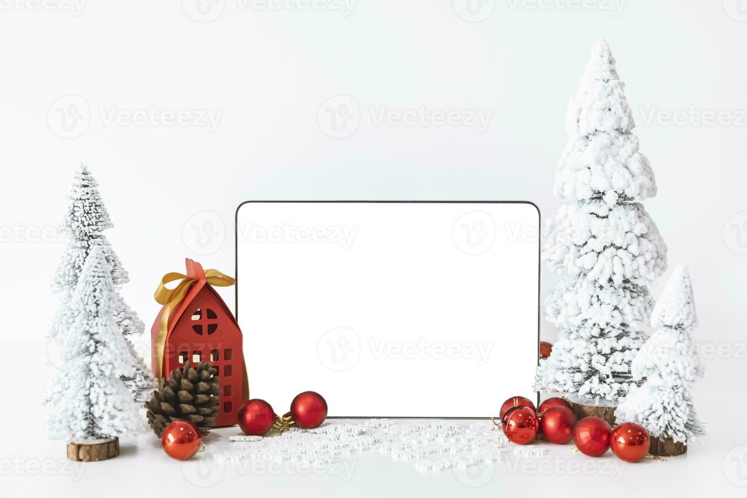Tapelet with a white screen mock-up and White calendar with a festive scene of a beautiful Christmas tree adorned, with Christmas balls, pine cones, and a red house gift box. photo