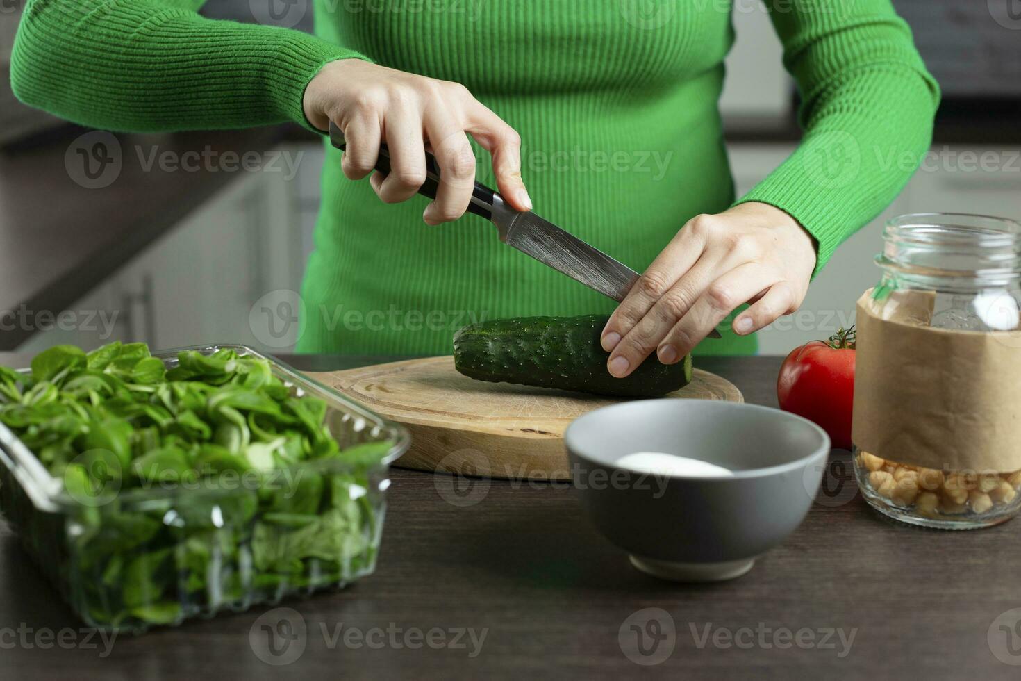Woman cuts cucumber for cooking vegetable salad. Home kitchen. photo