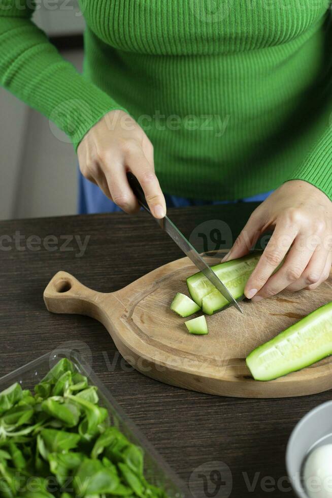 Woman cuts cucumber for cooking vegetable salad. Home kitchen. photo