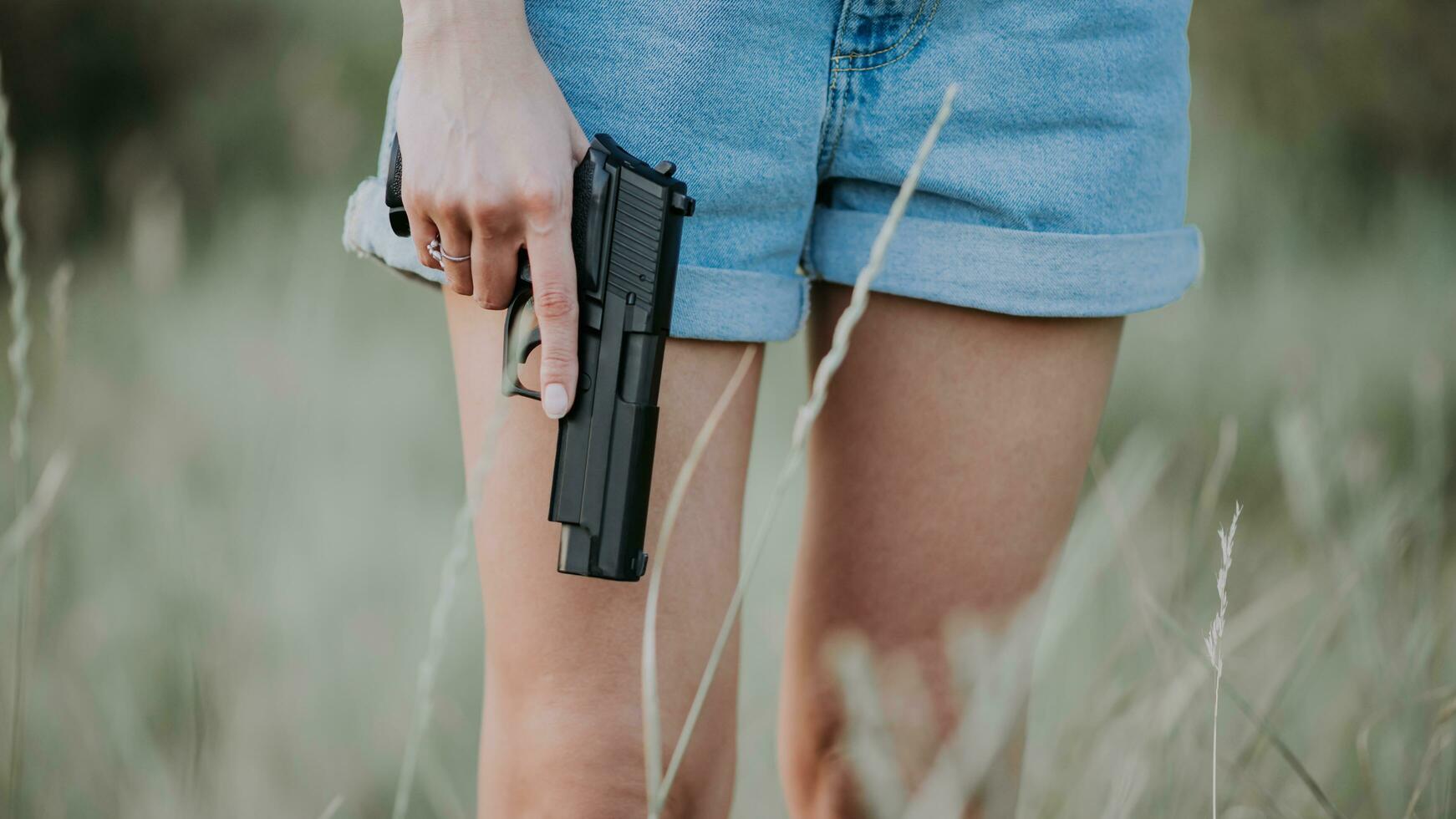 niña en mezclilla pantalones cortos y con un pistola en su mano posando en el campo. cerca arriba foto