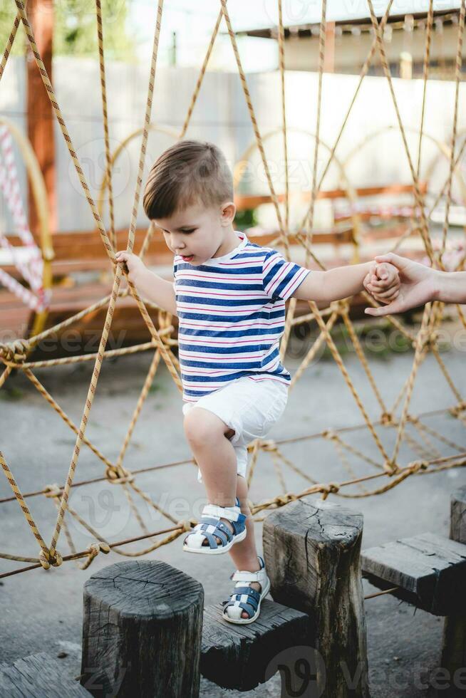 a little boy walks along a stretched wooden bridge in a rope town photo