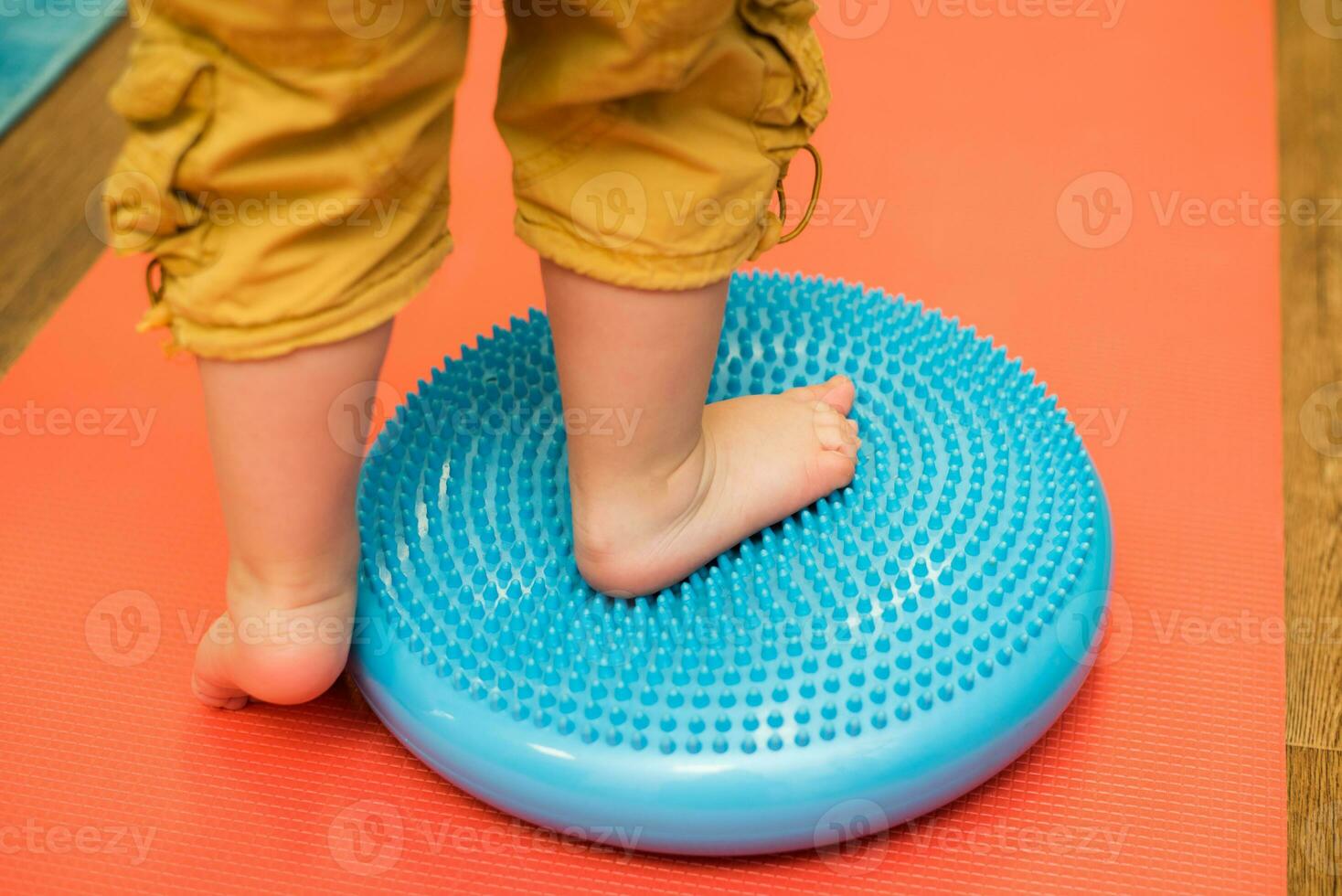 little kid massages his feet while standing on the rug photo