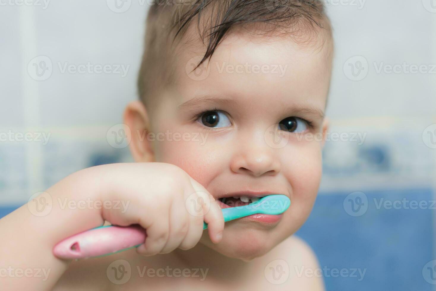 encantador bebé cepillado su dientes con un cepillo de dientes en el baño foto