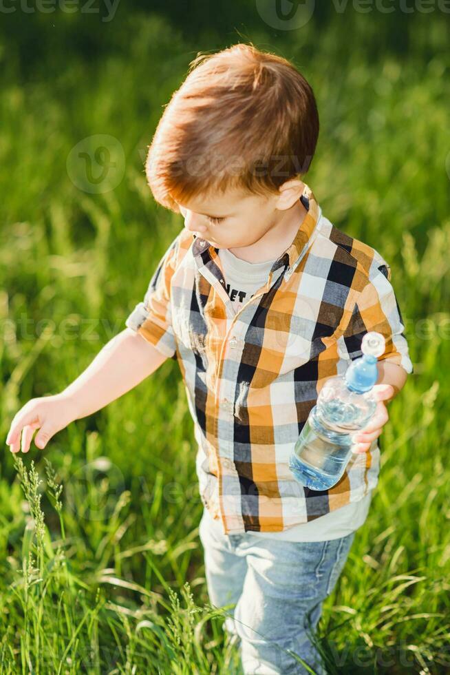 handsome boy drinks clear water from a bottle on a sunny day outside photo