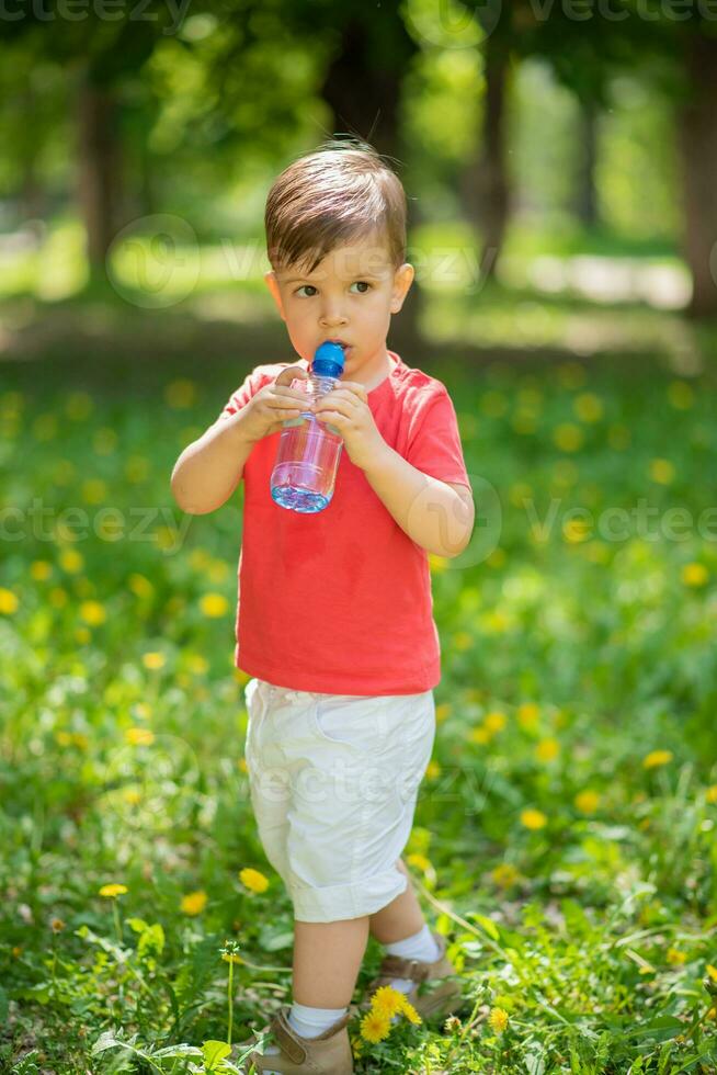 handsome boy drinks clear water from a bottle on a sunny day outside photo