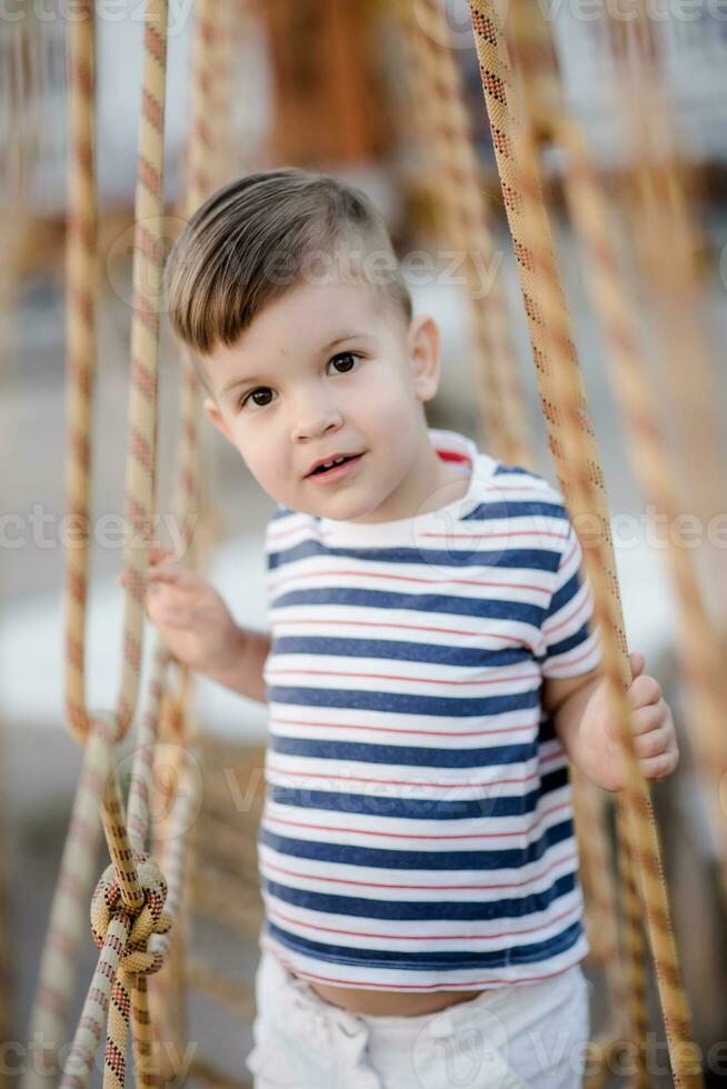 a little boy walks along a stretched wooden bridge in a rope town photo