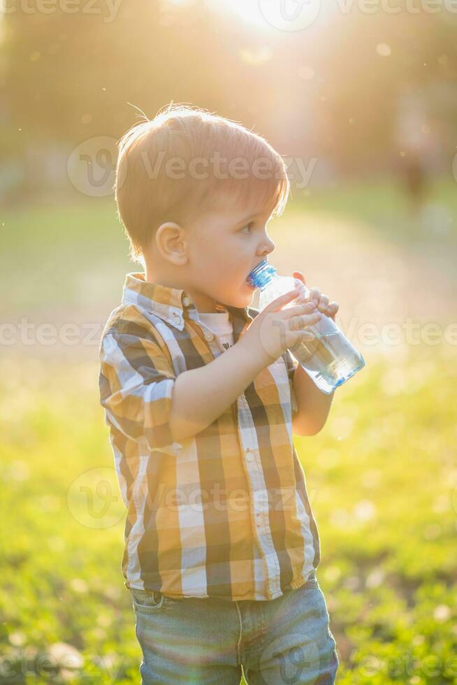 handsome boy drinks clear water from a bottle on a sunny day outside photo