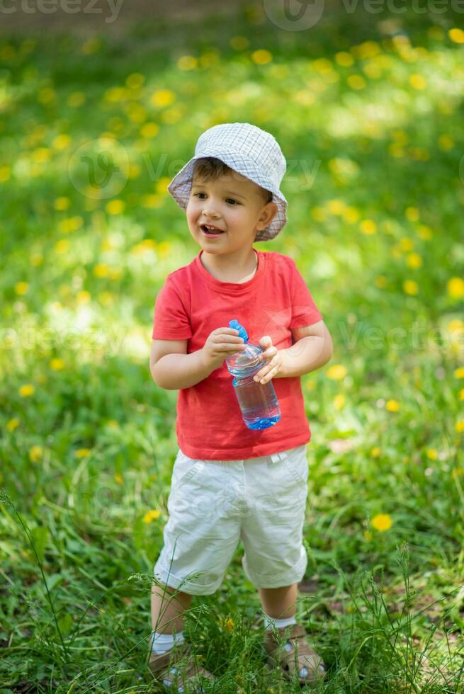 handsome boy drinks clear water from a bottle on a sunny day outside photo