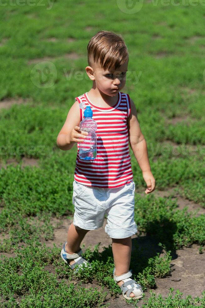 little boy drinks water from a bottle on a hot day playing on the meadow photo