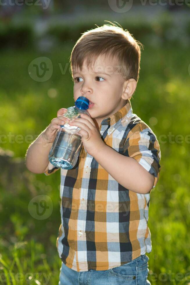 handsome boy drinks clear water from a bottle on a sunny day outside photo
