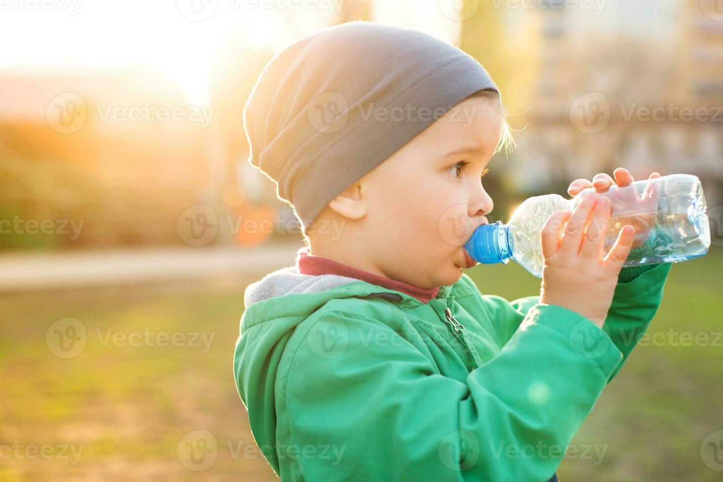 handsome boy drinks clear water from a bottle on a sunny day outside photo