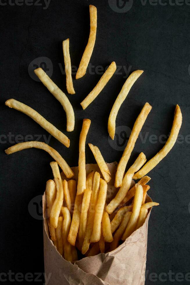 Appetizing crispy fries in an eco-friendly paper bag on black background. Hot american fast food. photo