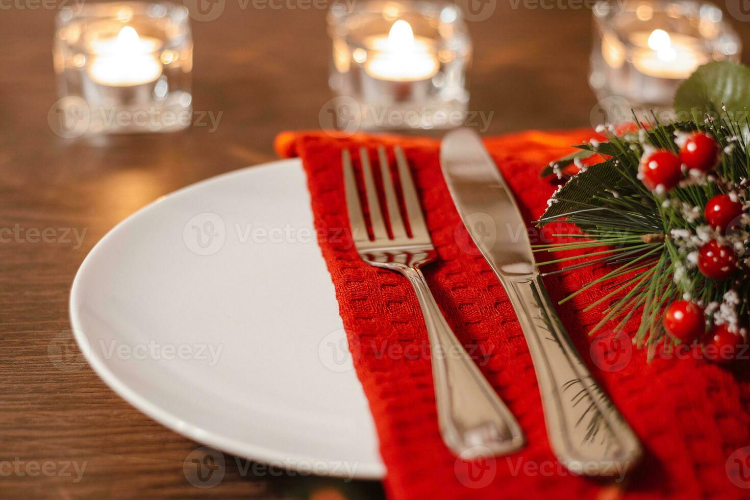 Christmas table setting. Plate and cutlery on napkin. Preparing for festive dinner. Candles burning on table on Christmas Eve. photo