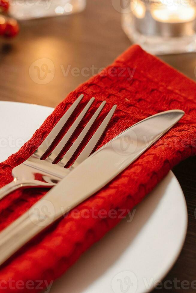 Christmas table setting. Plate and cutlery on red napkin. Preparing for festive dinner. Candles burning on table on Christmas Eve. photo