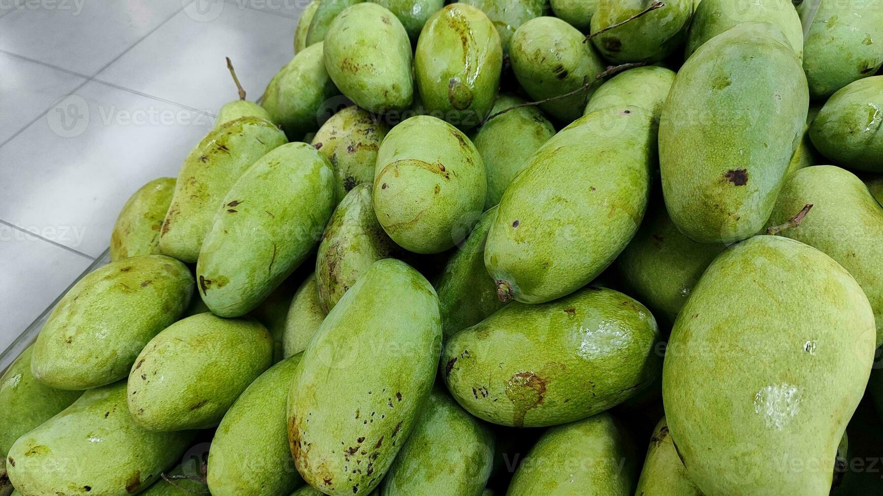 pile of big mango fruits on the shelf in local grocery supermarket, medium close up photo. photo