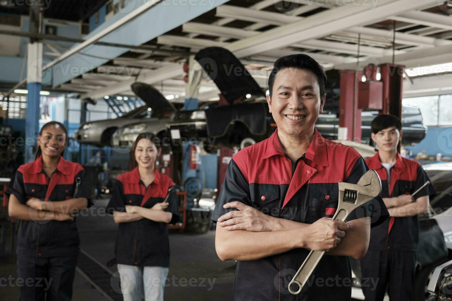 Portrait of professional workers team, male Asian supervisor arms crossed with fixing tools in front of mechanic colleagues, guarantee car repair jobs success with cheerful smiles at service garage. photo