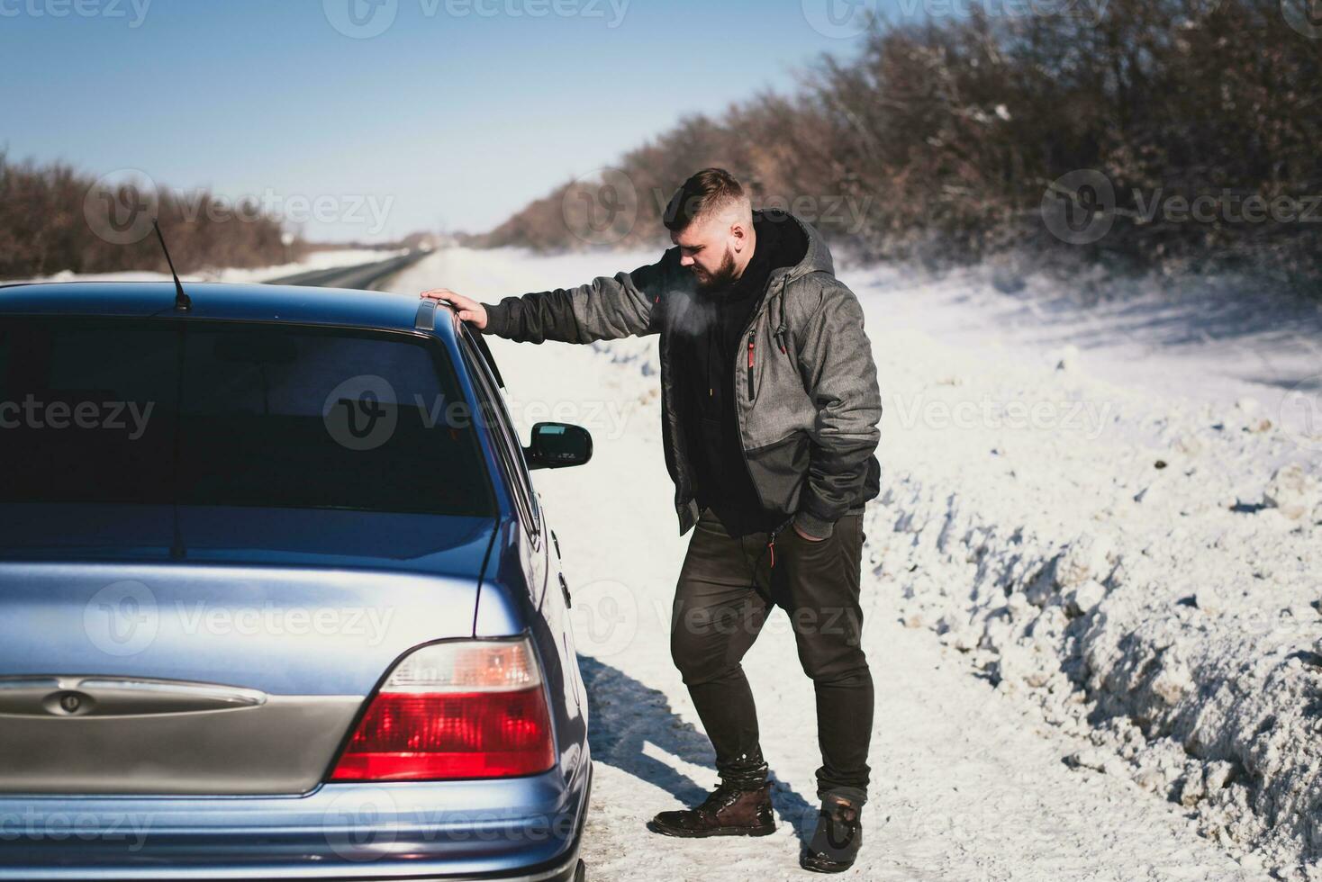 man stands near his broken car in winter photo