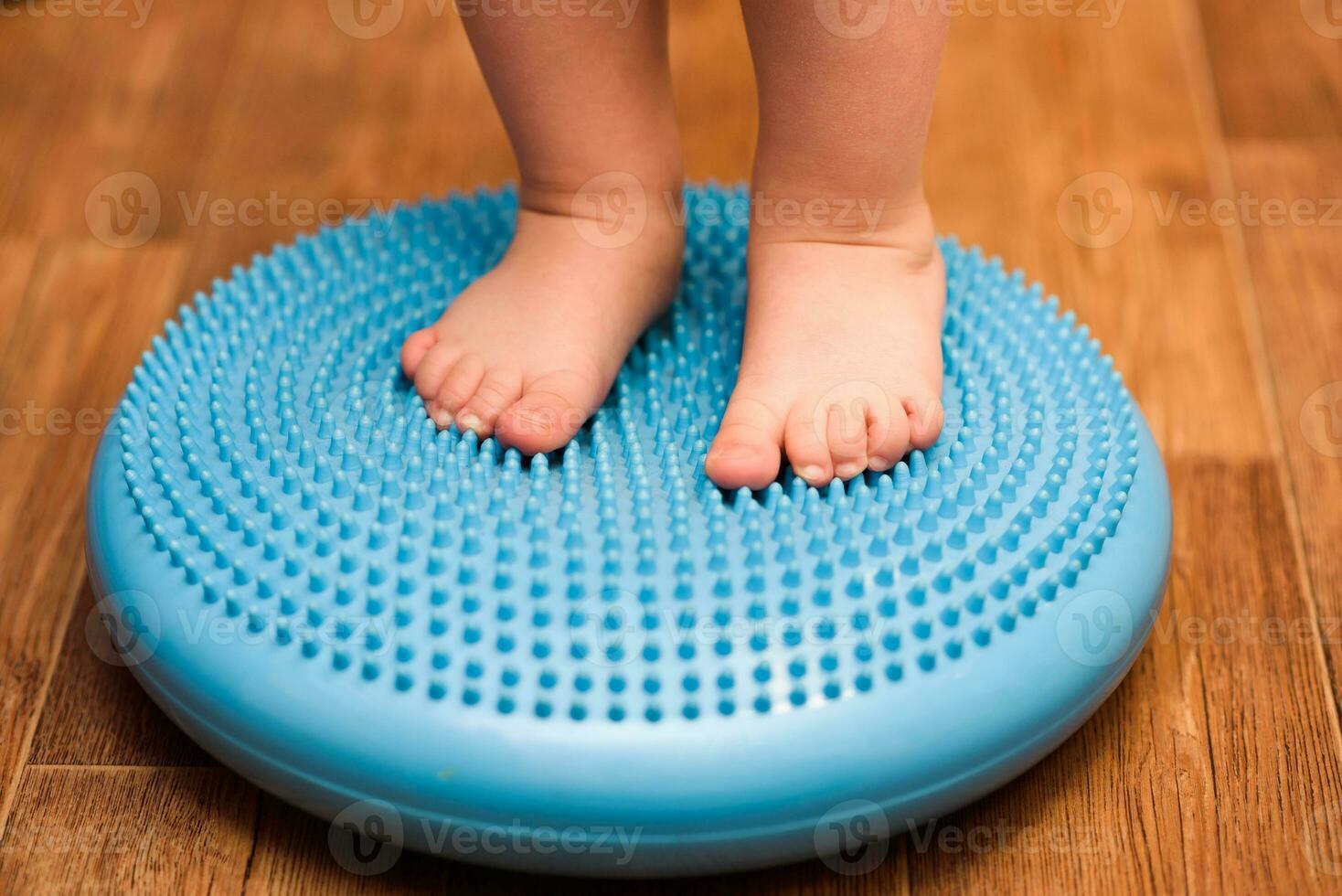 little kid massages his feet while standing on the rug photo