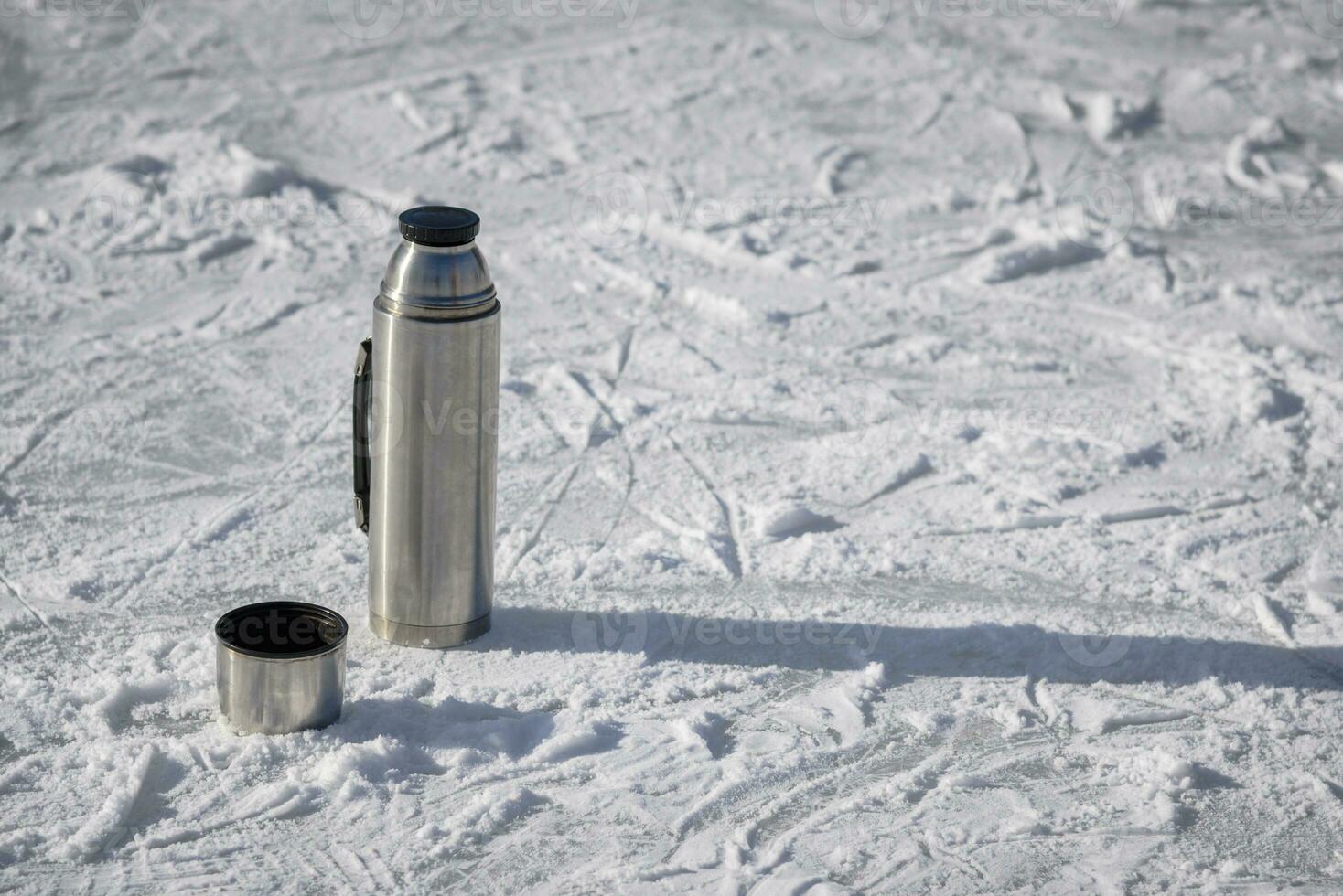 The thermos stands on ice with a cup of hot tea photo