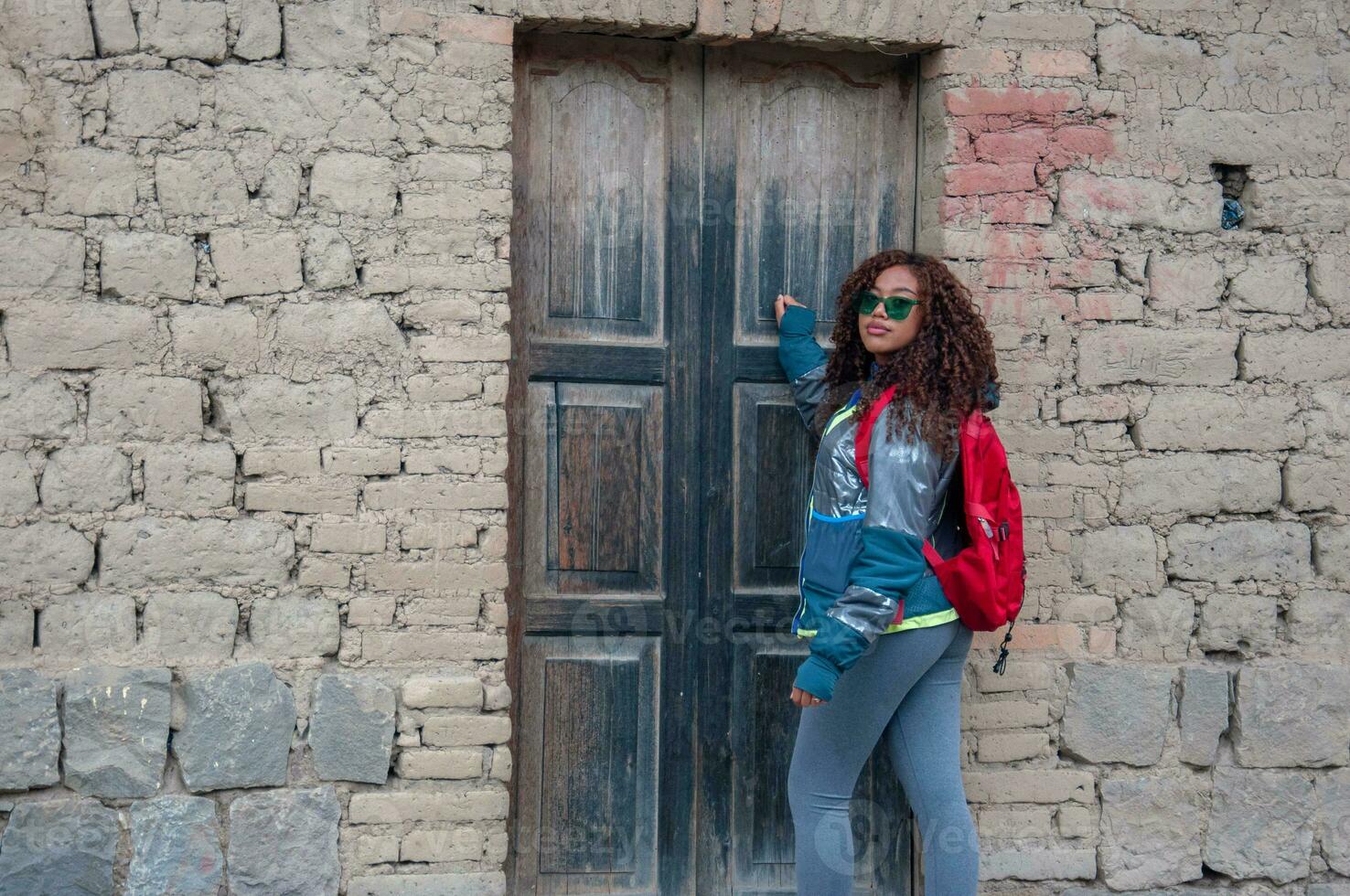 horizontal shot of a latin american woman in a rural house in south america with red backpack and mountain clothes. photo