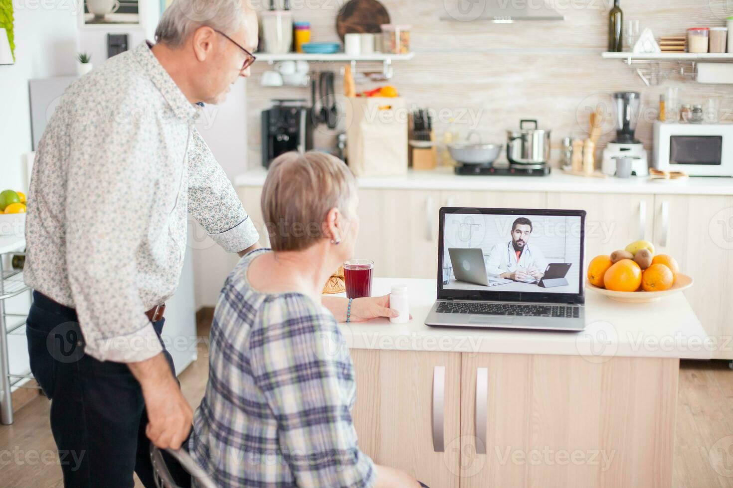 Doctor on telemedicine for senior couple. Video conference with doctor using laptop in kitchen. Online health consultation for elderly people drugs ilness advice on symptoms, physician telemedicine webcam. Medical care internet chat. photo