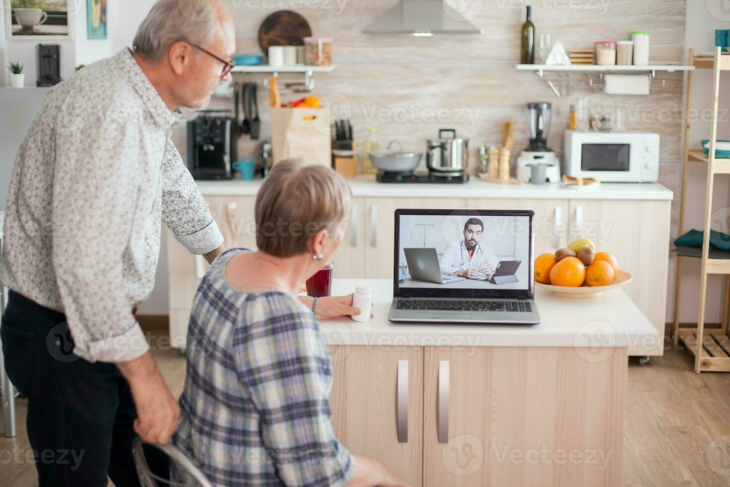 Senior couple during online medical check up from their home. Video conference with doctor using laptop in kitchen. Online health consultation for elderly people drugs ilness advice on symptoms, physician telemedicine webcam. Medical care internet chat photo