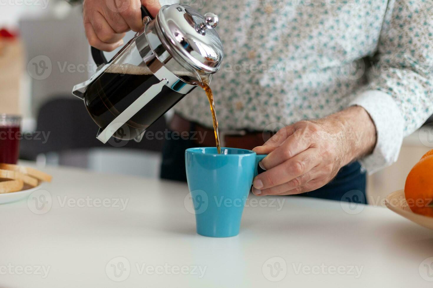 Elderly man using french press for coffee preparation and pouring it in mug. Senior person in the morning enjoying fresh brown cafe espresso cup caffeine from vintage mug, filter relax refreshment photo