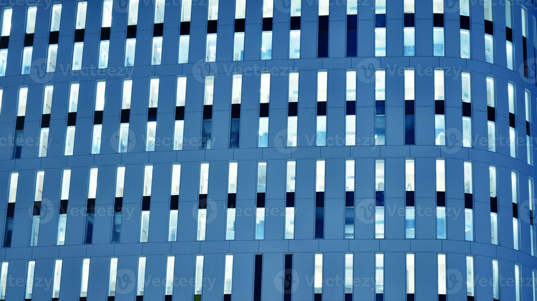 Pattern of office buildings windows illuminated at night. Glass architecture ,corporate building at night - business concept. Blue graphic filter. photo