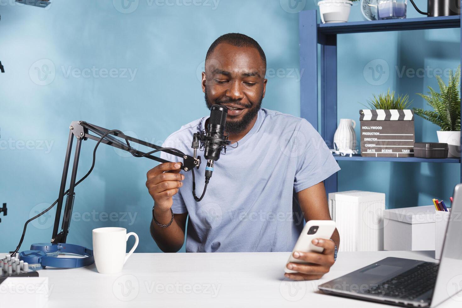 Smiling vlogger answering questions while holding smartphone and streaming online. Web content creator reading news on smartphone while recording video for internet channel photo