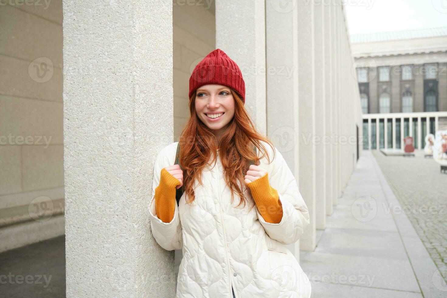 Female tourist in red hat with backpack, sightseeing, explores historical landmarks on her trip around europe, smiling and posing on street photo