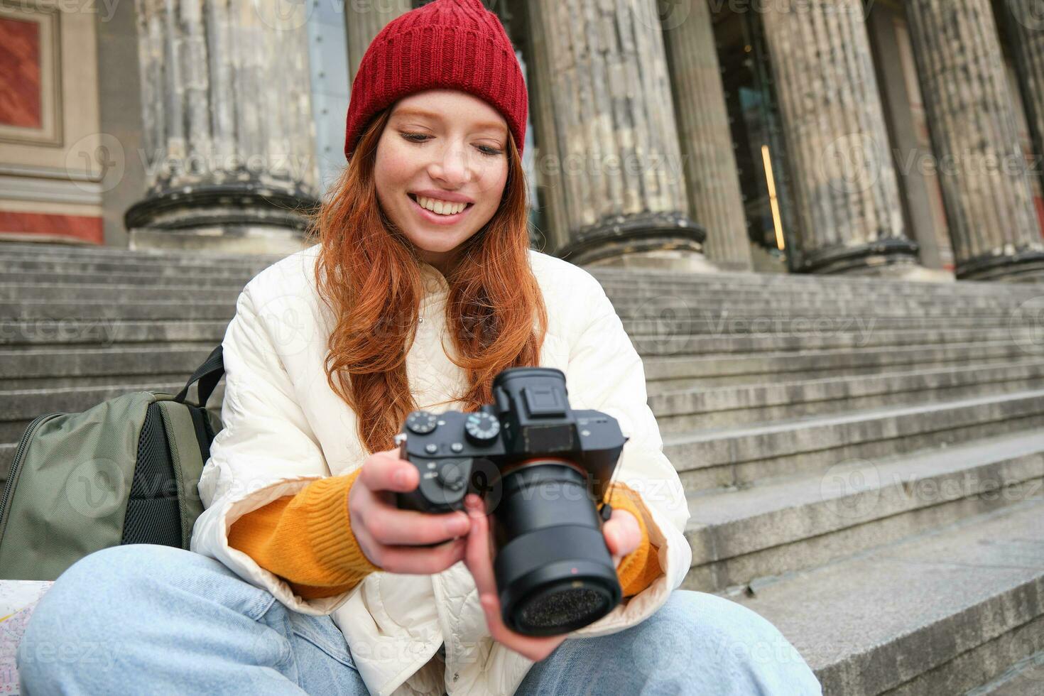 Portrait of young photographer girl, sits on stairs with professional camera, takes photos outdoors, making lifestyle shooting
