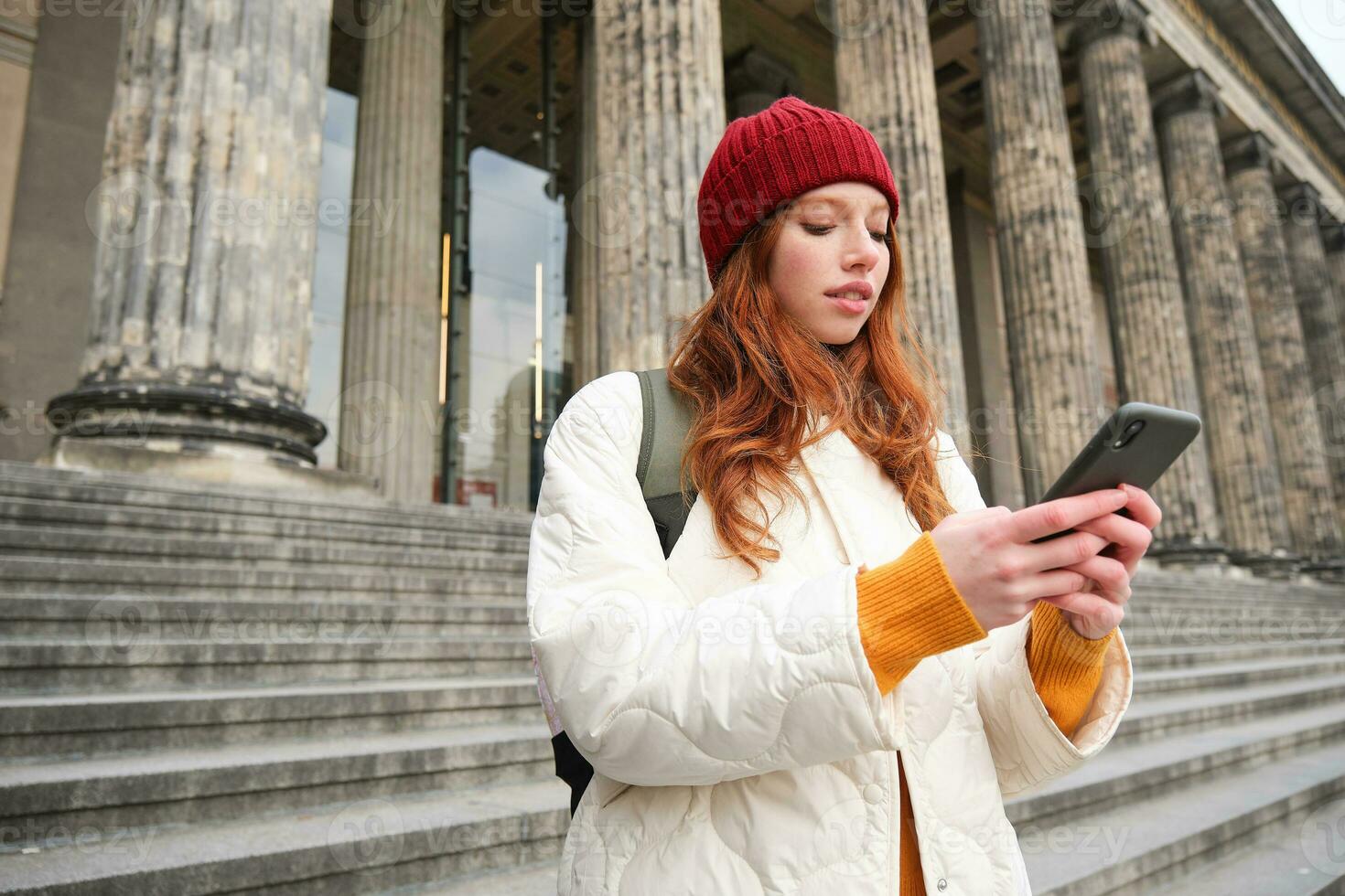 Portrait of young urban girl with backpack, using smartphone, walking around city, looking at map on mobile app, checking direction photo