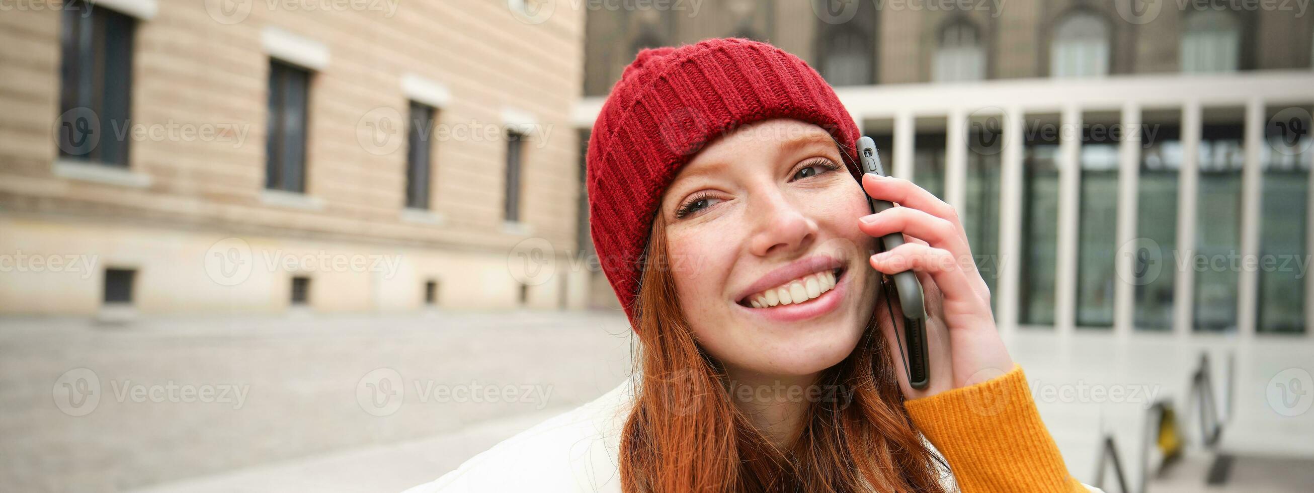 móvil conexión y personas concepto. contento pelirrojo mujer en sombrero, negociaciones en móvil teléfono, haciendo teléfono llamar, utilizando aplicación a llamada extranjero foto