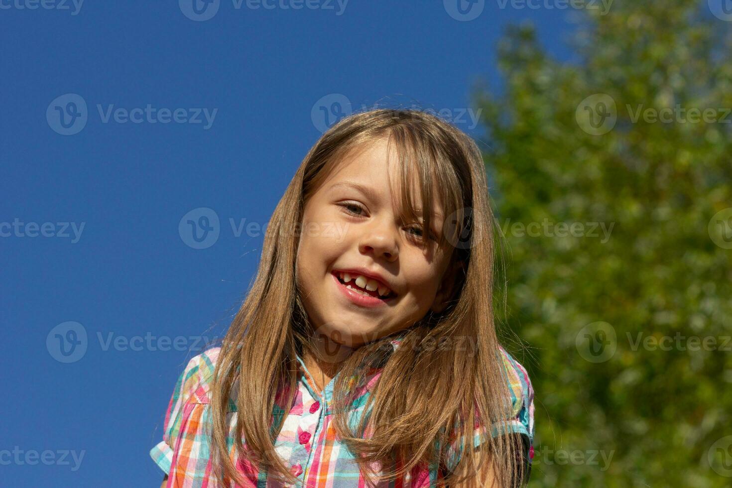 retrato de caucásico pequeño niña de 6 6 7 7 años sonriente y mirando a cámara terminado azul cielo foto