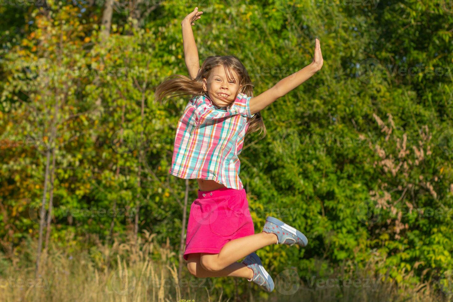 Happy beautiful caucasian child of 6 7 years jumping with the raised arms outside in summertime photo