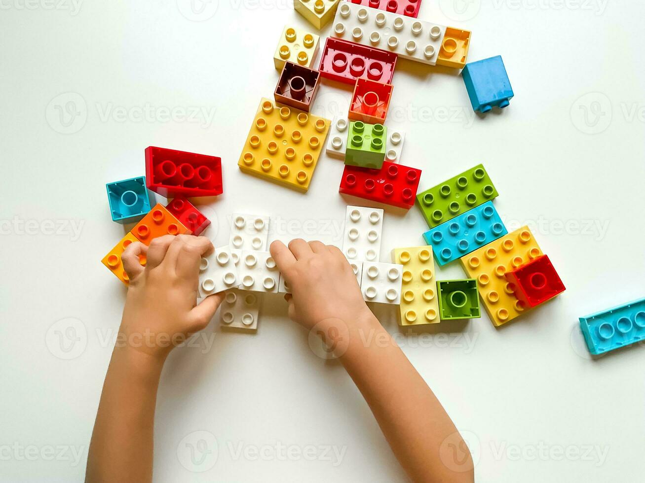Child playing with colorful building blocks on white background. Top view photo