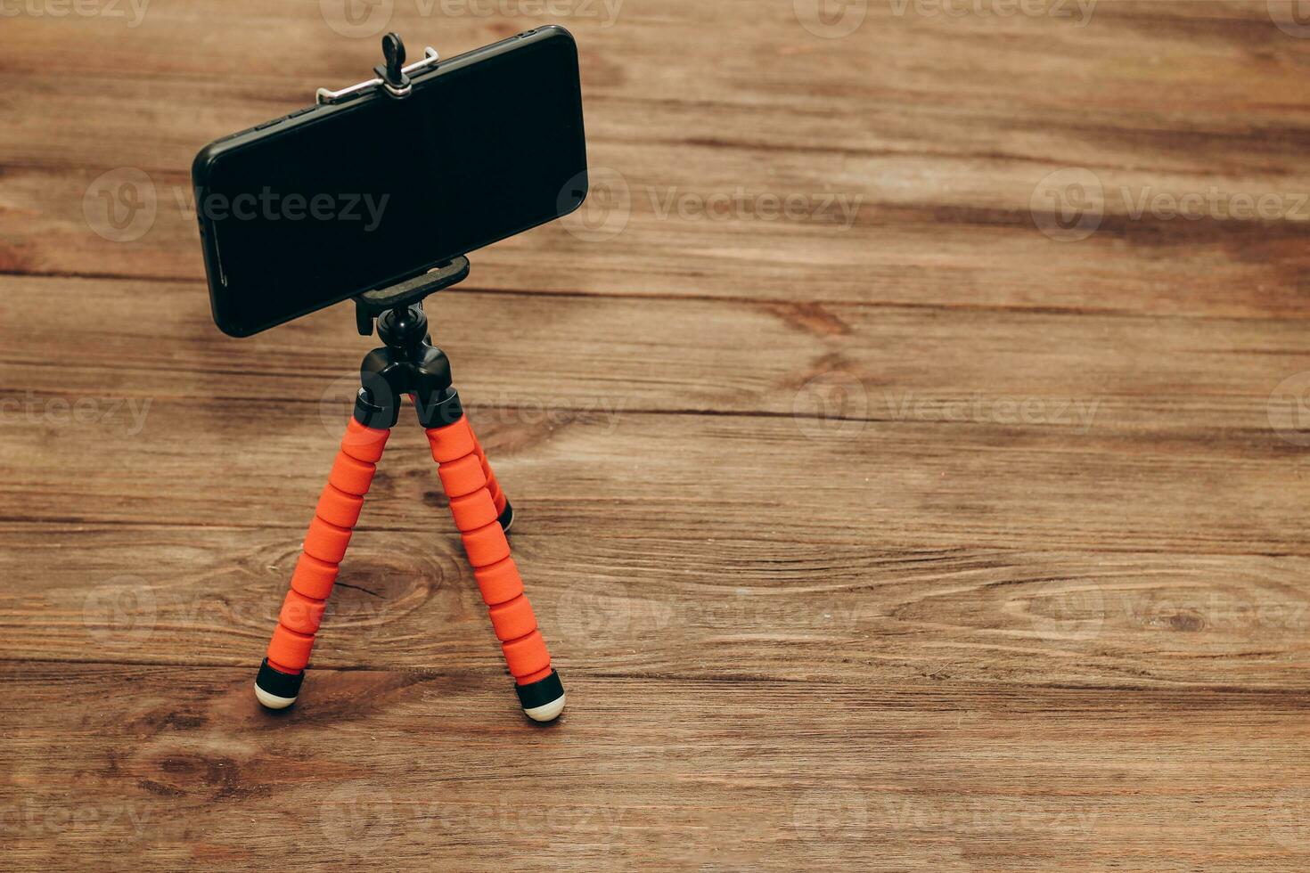 The phone stands on a manual monopod tripod for the camera on a wooden table.. photo