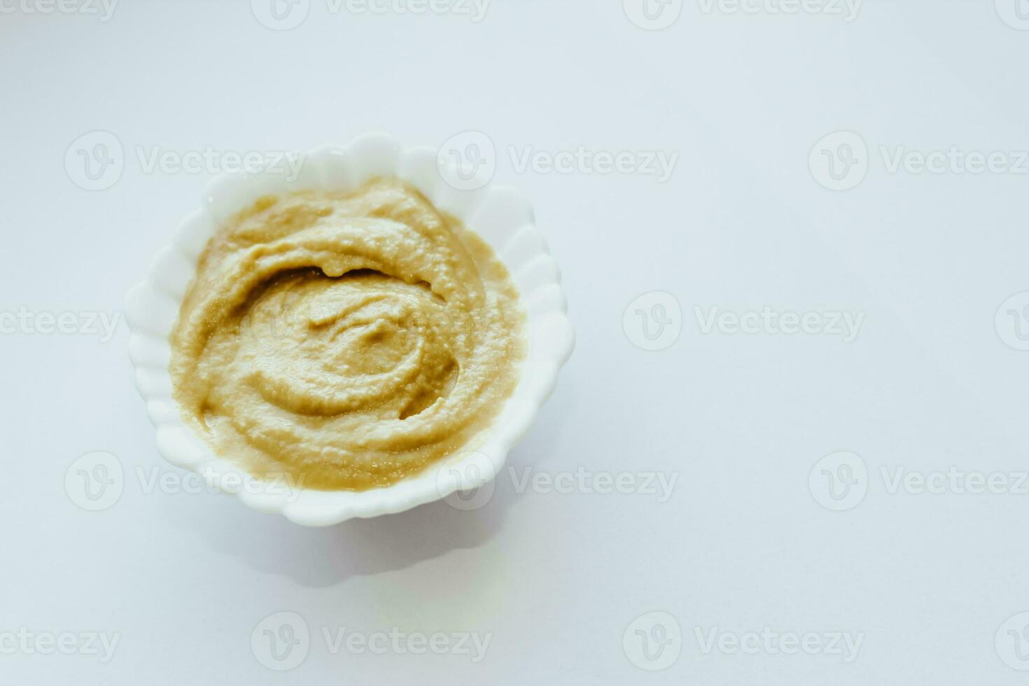 Mustard sauce in a white bowl on a white table. photo