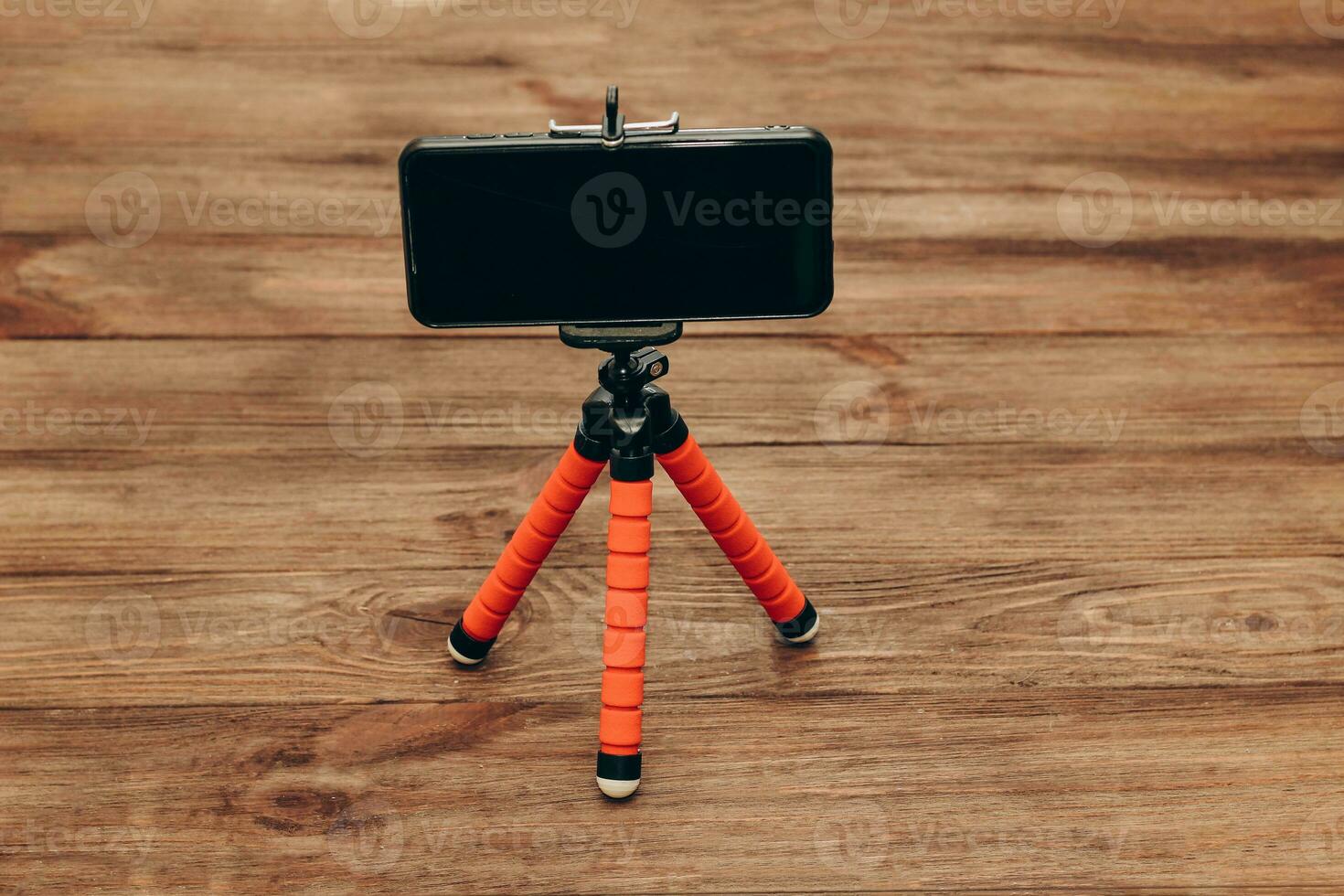 The phone stands on a manual monopod tripod for the camera on a wooden table.. photo
