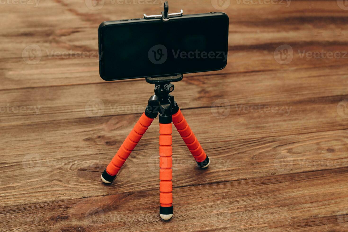 The phone stands on a manual monopod tripod for the camera on a wooden table.. photo