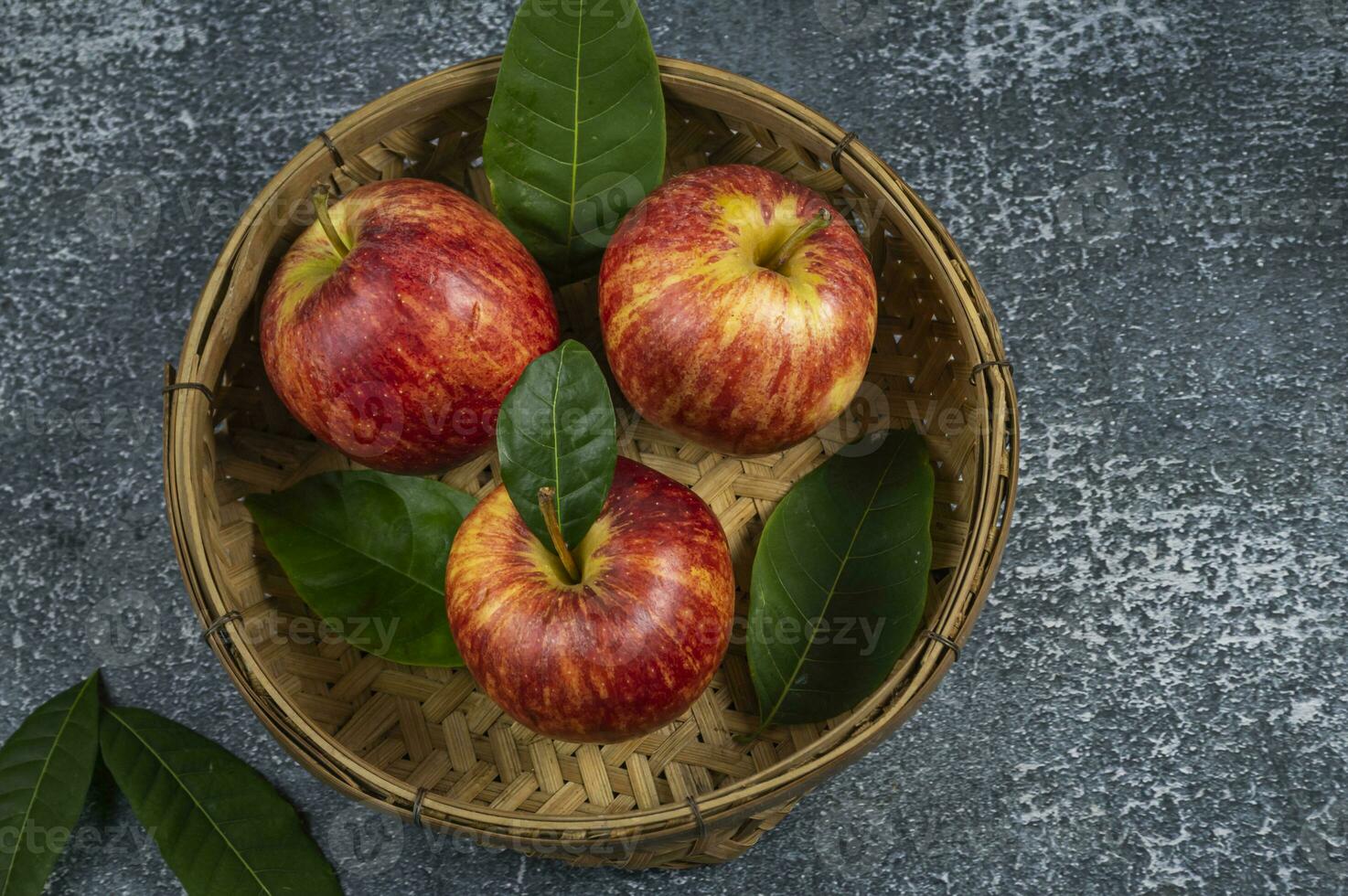 three apples in a basket with leaves photo