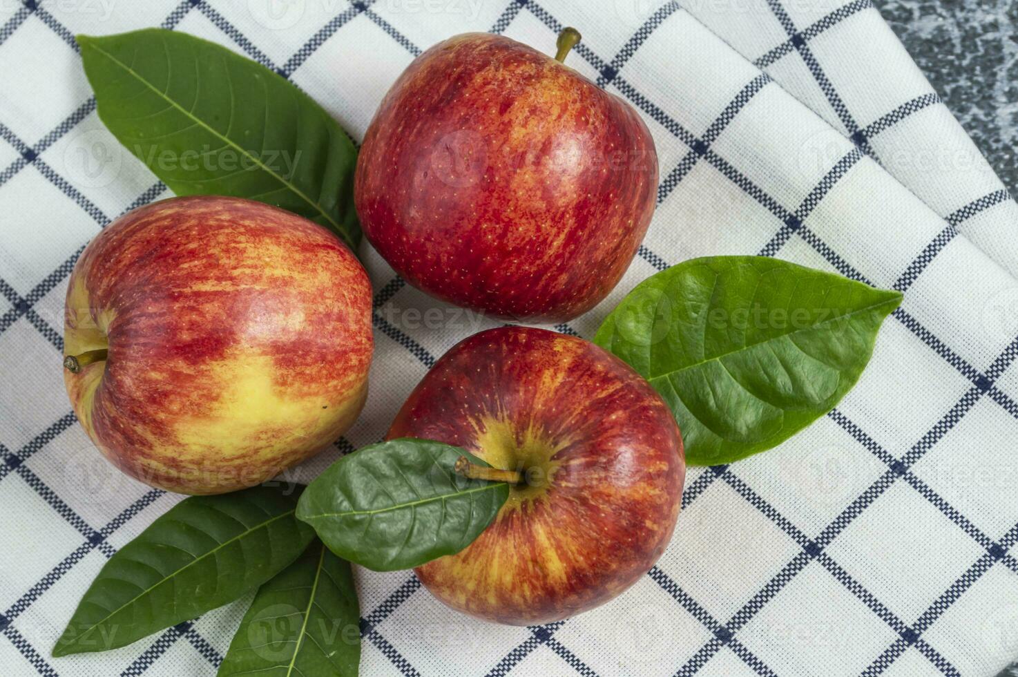 three apples with leaves on a checkered tablecloth photo