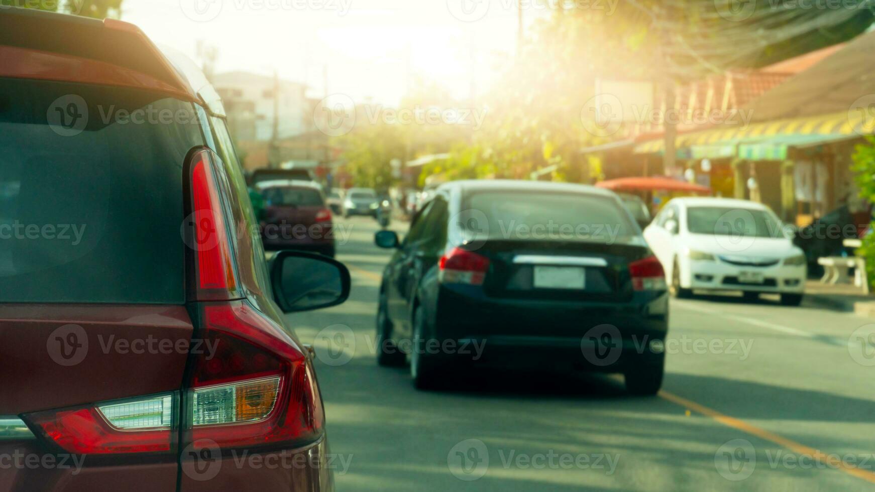 Rear side of red car driving on the asphalt road. Many car drivnig on the road with stop car beside road. Beside with small business building. background sunlight. photo